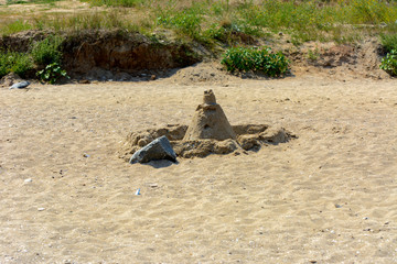 Sandy castle built by children with wet sand on the beach. Castles on the sand. Fun in the sand on the beach on a sunny day. Concept of summer vacation and travel.