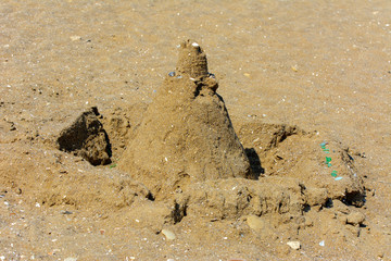 Sandy castle built by children with wet sand on the beach. Castles on the sand. Fun in the sand on the beach on a sunny day. Concept of summer vacation and travel.
