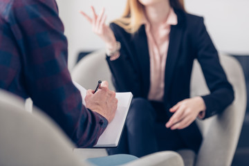 cropped image of businesswoman in suit giving interview to journalist and he taking notes in office