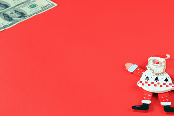 Toy Santa Claus on red background points to 100 dollar bills.  Money concept, Christmas, New Year gifts, travel and shopping.