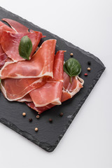 Italian prosciutto crudo or spanish jamon on a stone plate white background