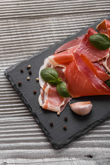 Italian prosciutto crudo or spanish jamon on a stone plate wooden background