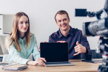 Obraz premium happy video bloggers recording vlog and pointing on laptop with blank screen in office