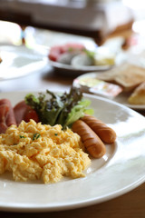 Breakfast scrambled egg with bacon sausage and salad on wood background