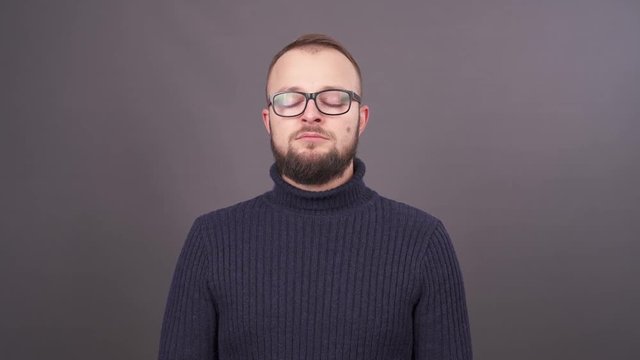 Close-up portrait of a bearded young snotty caucasian man in glasses , sneezing and blowing his nose. Isolated on grey background.