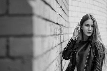 Young beautiful caucasian girl posing in a black leather jacket on a brick wall background.