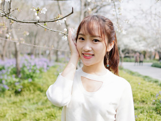 Outdoor portrait of beautiful young Chinese girl smiling among blossom cherry tree brunch in spring garden, beauty, summer, emotion, expression and people lifestyle concept.