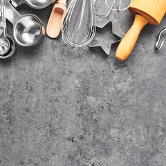 Kitchen utensils for baking or cooking background. Rolling pin, whisk, wooden spoon, cookie cutters and measuring spoons on dark grey concrete background with copy space. Top view. Square crop.