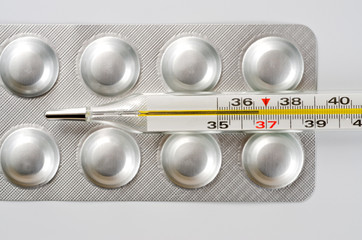 Plate with round medical tablets of silver color and glass thermometer