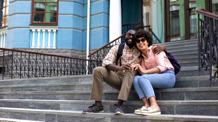 Happy student couple hugging, sitting on university building stairs, youth love