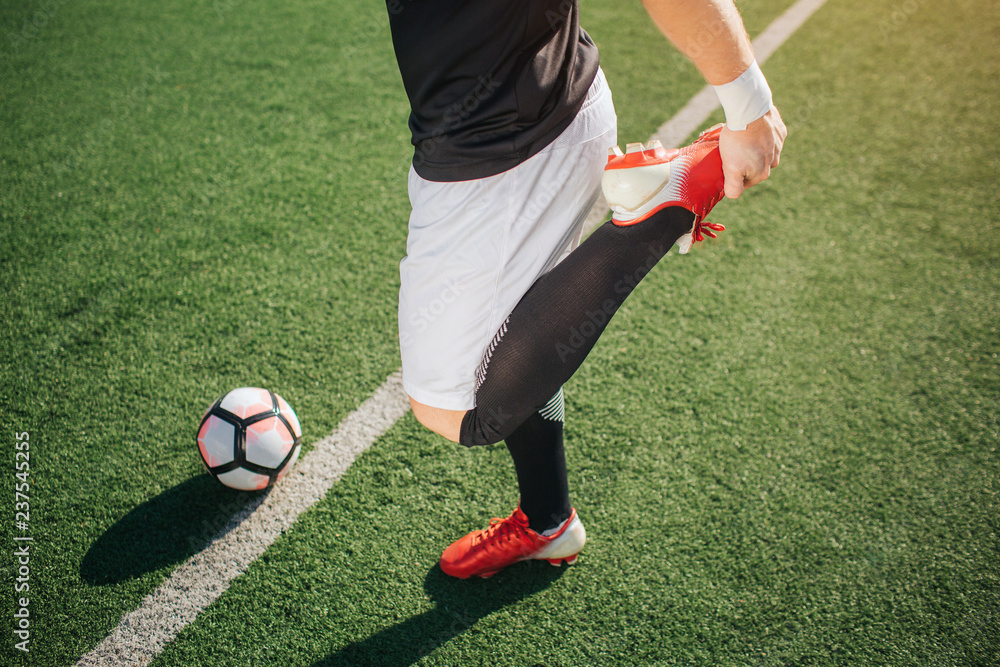 Canvas Prints Picture of football player warming up leg. He stretches it. Guy stand on green lawn at white line. Ball is behind it.