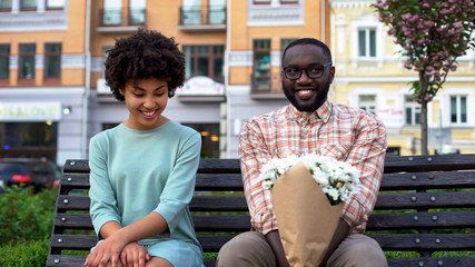 Embarrassed couple sitting on bench with flowers, first date, affection emotions