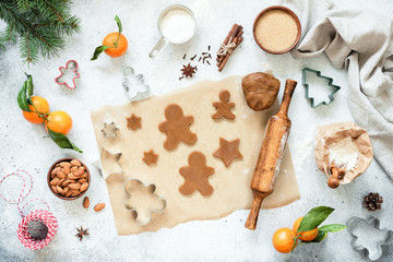 Fototapeta na wymiar Preparation of gingerbread cookies. Unbaked gingerbread cookies and cookie dough on parchment paper with Christmas decorations around. Top view, flat lay composition