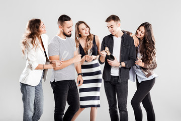 Company of friends in fashionable casual clothes stand together and smile. Guy opens a bottle of champagne