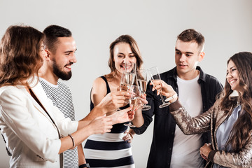 Girls and guys dressed in stylish casual clothes stand together and clink glasses with champagne. Party time