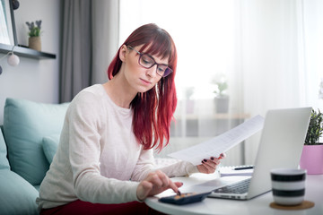 Young smiling woman working at home using laptop while sitting on sofa