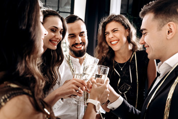 Сompany of friends dressed in stylish elegant clothes stand together and clink glasses with...