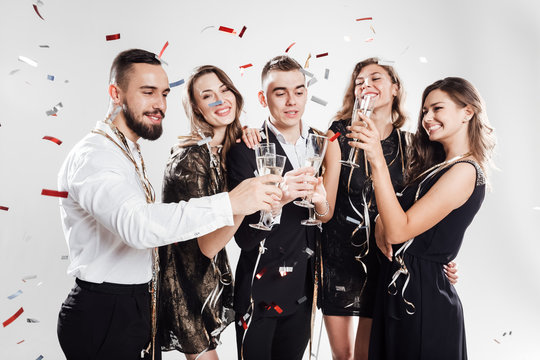 Girls and guys dressed in stylish elegant clothes stand together and clink glasses with champagne on the white background confiture around. Party time