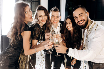 Сompany of beautiful young girls and guys dressed in stylish elegant clothes stand together and clink glasses with champagne. Party time