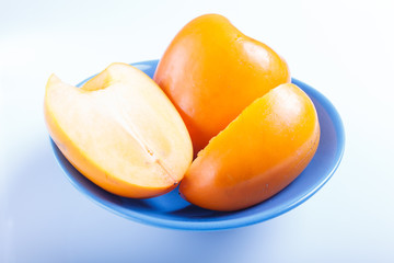 Ripe orange persimmon in a blue plate isolated on white background.