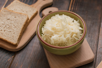 Sauerkraut in a plate and a piece of bread on a wooden background.
