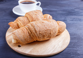 two croissants with cup of coffee on white plate on black wooden background