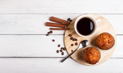 two carrot muffins with cup of coffee on wooden kitchen board on white wooden background