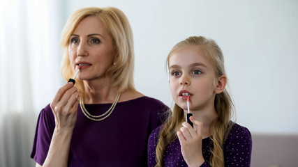 Beautiful granny and little granddaughter applying lipstick, preparing for party