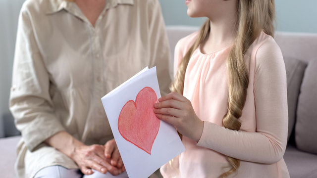 Smiling Granddaughter Gifting Handmade Greeting Card With Heart To Grandmom