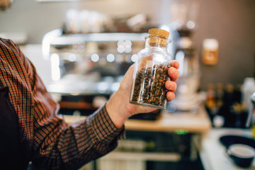 Man hold glass on coffee beans in hand. He stands inside in kitchen. Cut view.