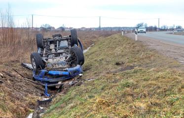 Car crash. Blue car overturned on the road. Transport traffic accident.