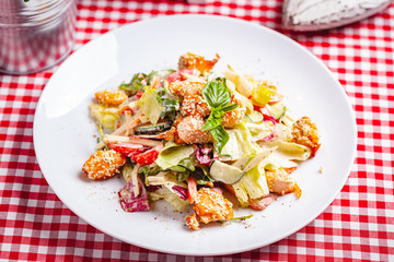 Salad with salmon, vegetables and mixed greens on white plate. Close up