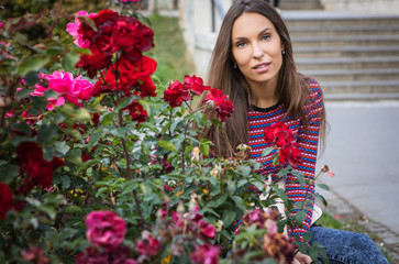 Portrait of beautiful young girl near flower bed of roses.