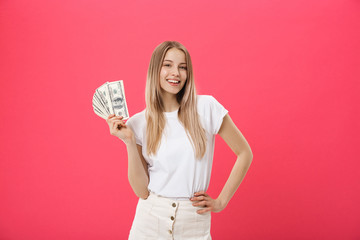 Portrait of a cheerful young woman holding money banknotes and celebrating isolated over pink background
