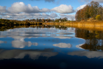 Autumn landscape with colorful trees, yellow grass and river. Reflection in river
