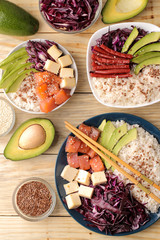 poke bowl Hawaiian food. a plate of rice, salmon, avocado, cabbage and cheese. next to sesame and fresh avocado on a natural wooden table top view.