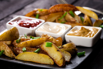 Homemade organic vegetable vegan vegetarian baked potato wedges with chives and sauces.