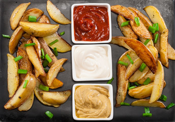 Homemade organic vegetable vegan vegetarian baked potato wedges with chives and sauces.