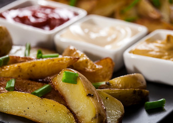 Homemade organic vegetable vegan vegetarian baked potato wedges with chives and sauces.