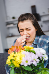 girl with allergy sneezing and holding bouquet of flowers at home
