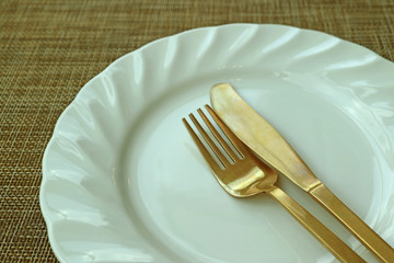 Closed Up White Ceramic Plate and Brass Cutlery on Beige Luncheon Mat 