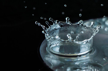Close up, extreme macro. High speed photography. A drop of water when it strikes the surface of the disk forms a crown. Dark background.