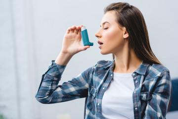 young woman using inhaler while suffering from asthma at home - obrazy, fototapety, plakaty