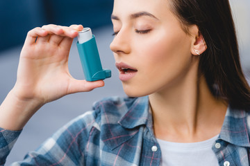 close-up view of young woman using inhaler while suffering from asthma - obrazy, fototapety, plakaty