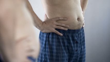 Naklejka premium Aged man looking at his belly and remembering his pumped up figure and press