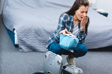 high angle view of girl with allergy sneezing while holding container from vacuum cleaner with dust