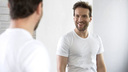 Cheerful man looking at reflection in mirror, motivating for success during day