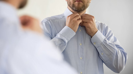 Serious man buttoning his shirt in optimistic mood, getting ready for work
