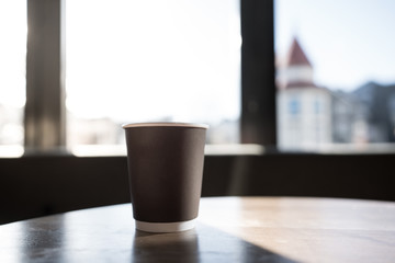 Isolated coffee in paper cup setting on wood teak table in cafe with natural light through the window/ Morning time /space for advertising / standalone cup /close up object with background /