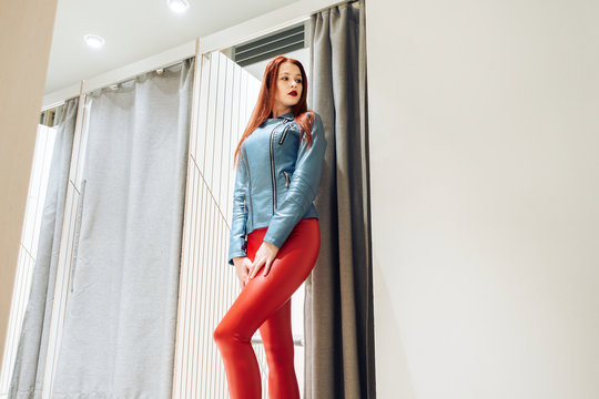 slim girl with redheads chooses clothes. woman in red leather pants posing in fitting room bottom view